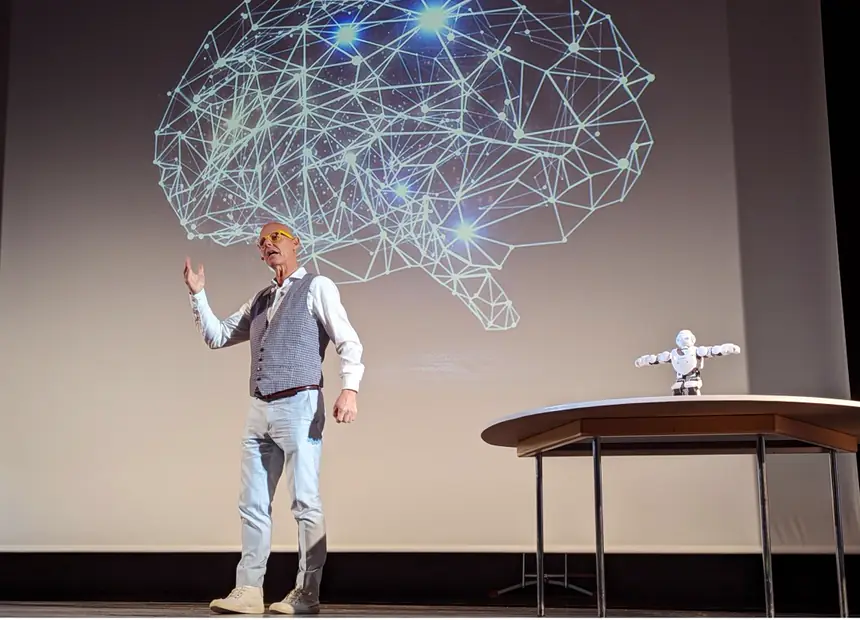 Frank Astor on stage in front of a projected brain graphic, with a humanoid robot beside him